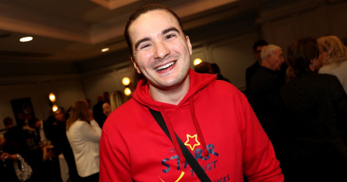 A young person smiling, wearing a red hoodie with the logo of the Starr Trust on